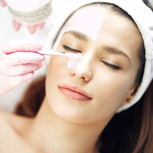 Female lying down with closed eyes and receiving a face mask application