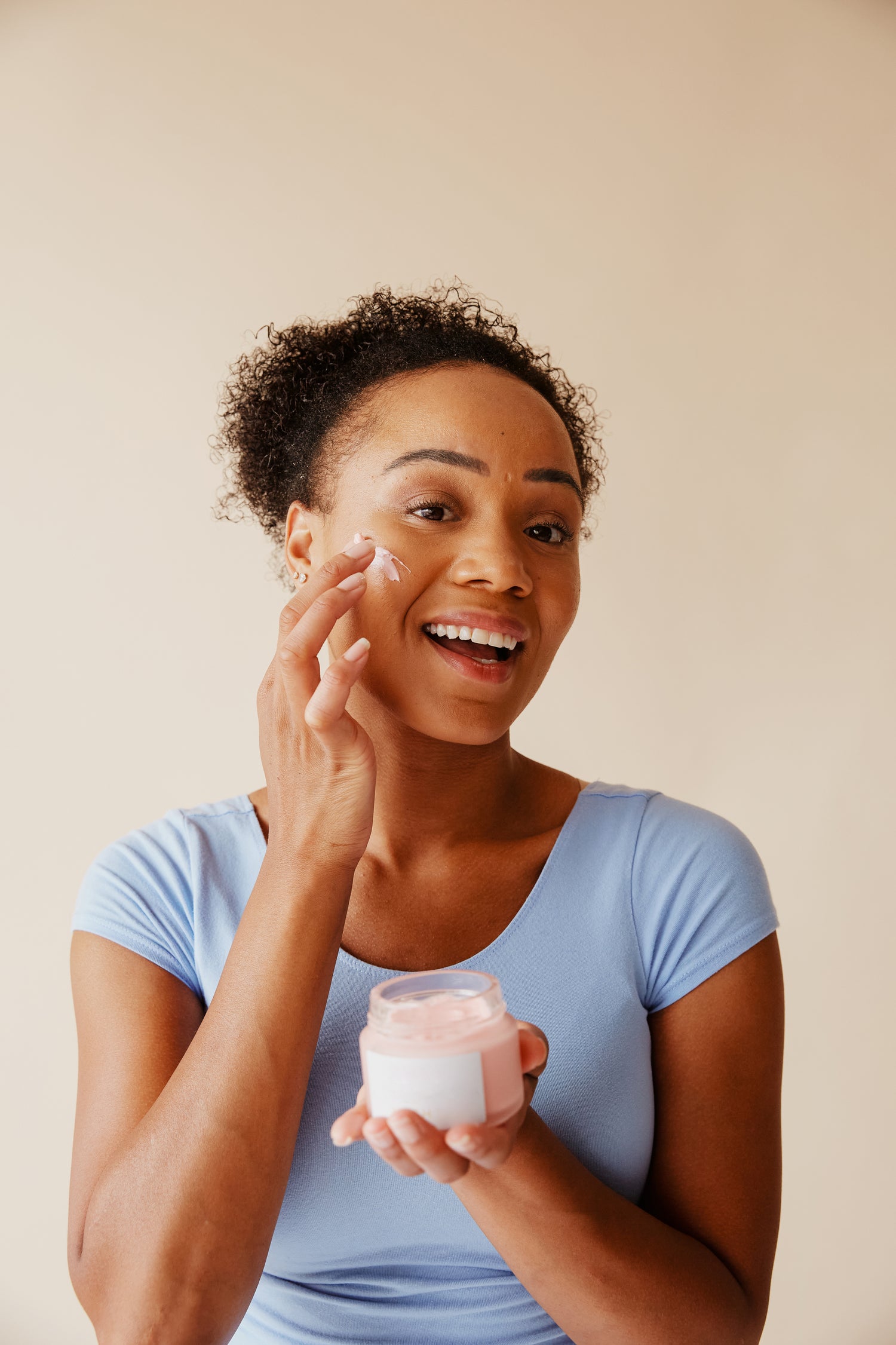 A women smiles and applying face moisturizer